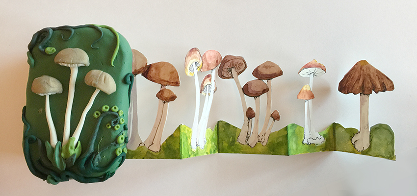 A mint tin covered in polymer clay decorated with realistic looking mushrooms holds a concertina-style row of water color mushrooms.